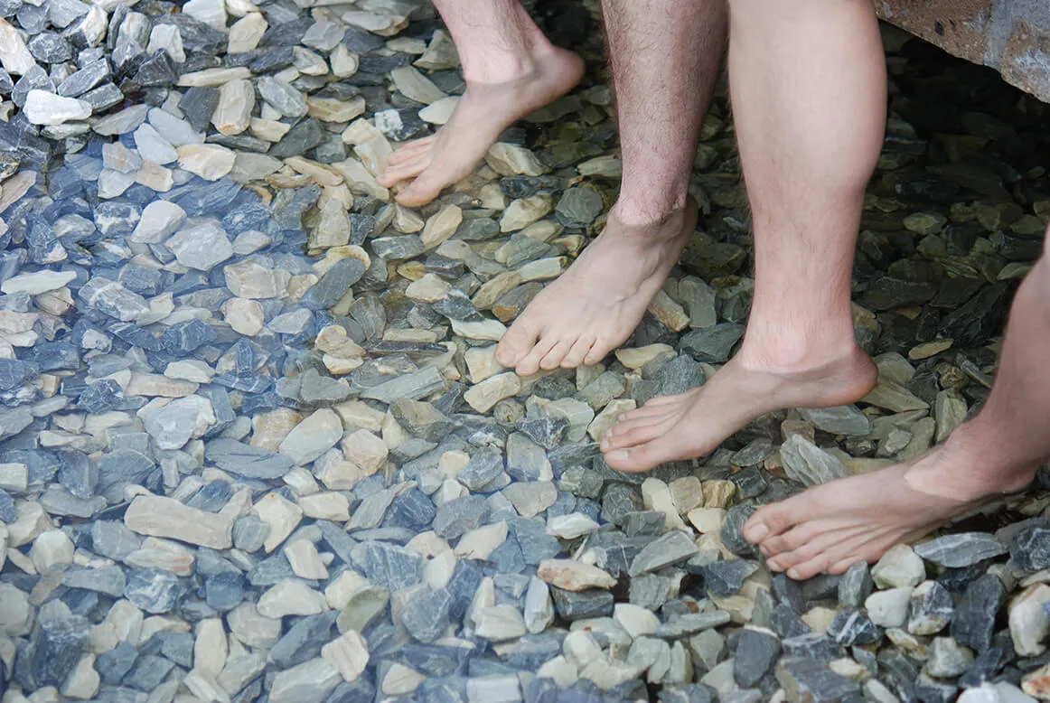Barfuß beim Wassertreten über Kieselsteine in einem flachen Wasserbecken